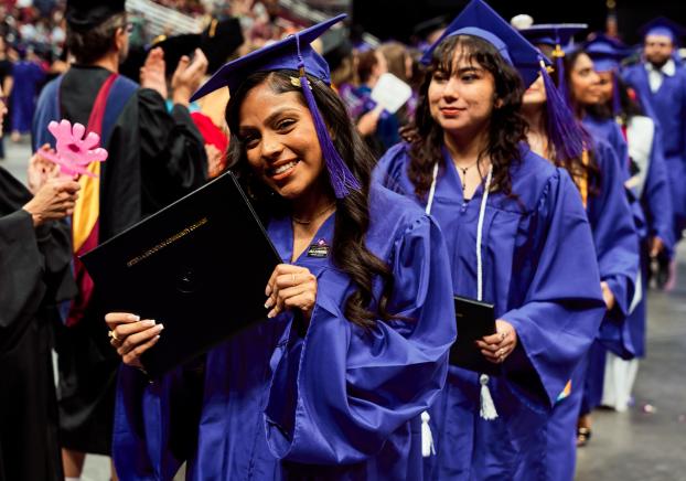 student at graduation holding up diploma to camera
