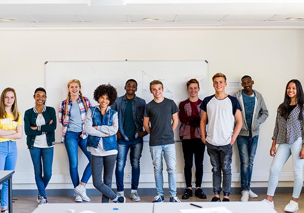 A group of young adults standing against a wall and smiling.
